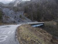 a bridge spanning the mountains to pass over a dirt road with a rock hill on either side