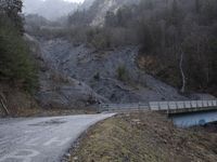 a bridge spanning the mountains to pass over a dirt road with a rock hill on either side