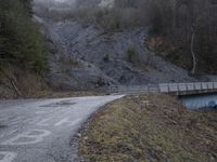 a bridge spanning the mountains to pass over a dirt road with a rock hill on either side