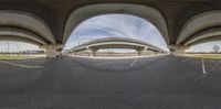 a fish eye lens picture of the view of a bridge from a parking lot underneath