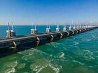 a bridge over the ocean with construction equipment in the background and two people walking on it