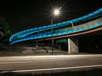 the bridge on a city street has bright blue lights on it's walkway above it