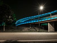 the bridge on a city street has bright blue lights on it's walkway above it