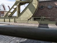 there is an unusual shaped bridge going across a brick street with buildings in the background