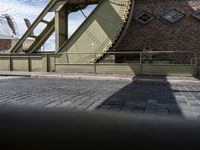 there is an unusual shaped bridge going across a brick street with buildings in the background