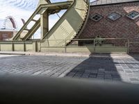 there is an unusual shaped bridge going across a brick street with buildings in the background