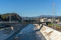 a bridge over a river in a rural area with power lines in the background and mountains