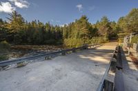 a bridge across a small river next to trees and dirt ground with benches in front