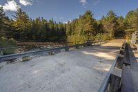 a bridge across a small river next to trees and dirt ground with benches in front