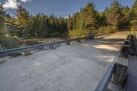 a bridge across a small river next to trees and dirt ground with benches in front