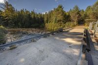 a bridge across a small river next to trees and dirt ground with benches in front