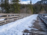 a wooden bridge with snow on top and pine trees on the side of it in the background