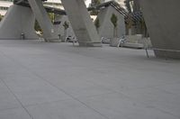a few chairs and benches sit under a bridge with large concrete pillars in the background