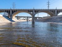 bridge spanning river with water next to it and traffic over road crossing to right of image