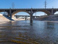 bridge spanning river with water next to it and traffic over road crossing to right of image