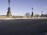 the statue is on the side of the bridge and has three street lamps on each end