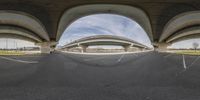 a fish eye lens picture of the view of a bridge from a parking lot underneath