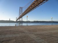 a long bridge that spans over water with a boat in the background, seen from the sidewalk area