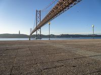 a long bridge that spans over water with a boat in the background, seen from the sidewalk area