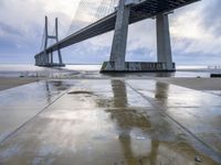 the view of a bridge from the ground of the water below it and over the pier