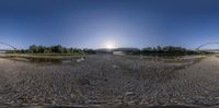 the view from a fish eye lens of a sandy river with many rocks and a bridge