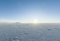 a lone person walks across the snow covered ground outside with a bright sun in the background