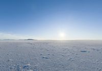 a lone person walks across the snow covered ground outside with a bright sun in the background