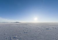 a lone person walks across the snow covered ground outside with a bright sun in the background