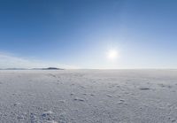 a lone person walks across the snow covered ground outside with a bright sun in the background