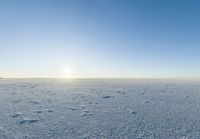 a lone person walks across the snow covered ground outside with a bright sun in the background