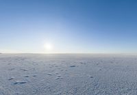 a lone person walks across the snow covered ground outside with a bright sun in the background