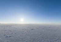 a lone person walks across the snow covered ground outside with a bright sun in the background