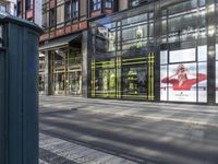 the large outdoor store front on the street corner is painted a bright yellow stripe and features advertises on glass and a poster