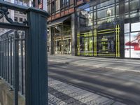 the large outdoor store front on the street corner is painted a bright yellow stripe and features advertises on glass and a poster