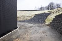 the view from behind two road spaces next to buildings in the background, some dry grass and yellow grass, a rock wall is outlining, and an open air conditioning