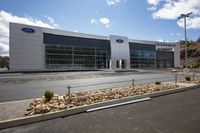 a car dealership with large windows and rocks in the front of it, outside on a sunny day