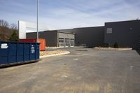 an outside dumpster in a parking lot with a grey building and blue doors behind it