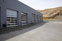 a large grey building with garages and windows with hills in the background at top