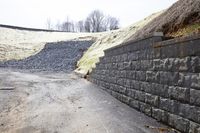 a concrete block wall on the side of a road near a cement block wall along with a pile of rocks