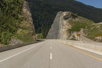 an empty highway in the mountains by some cliffs and forest on the right bank of the road