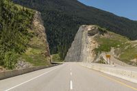 an empty highway in the mountains by some cliffs and forest on the right bank of the road