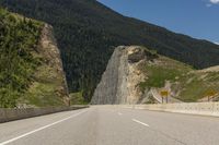 an empty highway in the mountains by some cliffs and forest on the right bank of the road