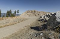 there is a bike rider on a paved dirt road through rocky area near a mountain