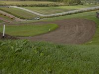 a dirt track surrounded by lush green field in countryside area with cars parked across path