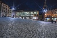 an image of people walking around a square at night near a large building and clock tower