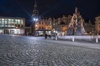 an image of people walking around a square at night near a large building and clock tower