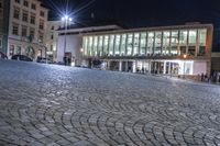 an image of people walking around a square at night near a large building and clock tower