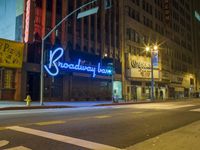 the neon sign of broadway in new york is lit up at night by a city traffic light