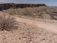 a person riding on a dirt road by a desert area near mountains and rocks and shrubs