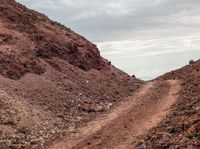 a dirt road near the mountain with hills in the background and sparse cloud filled sky